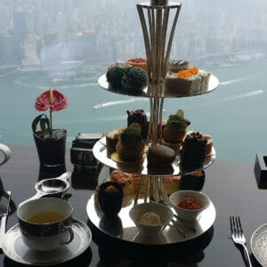 An afternoon tea set on a 3-tier silver tray in front of a window overlooking Hong Kong harbor.