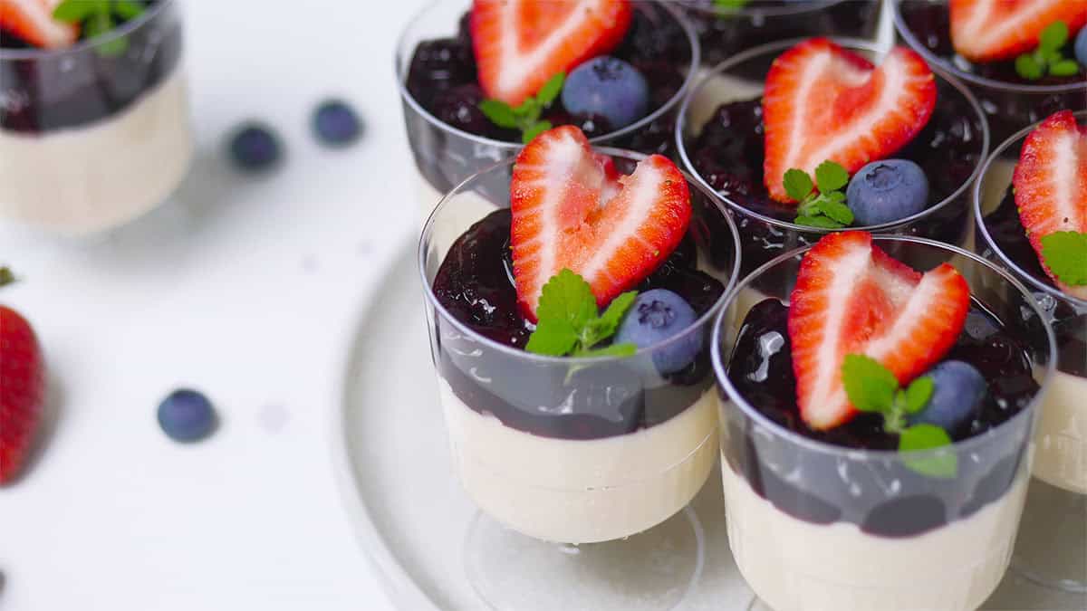Close up of a group of mini berry panna cottas served in disposable cups. 