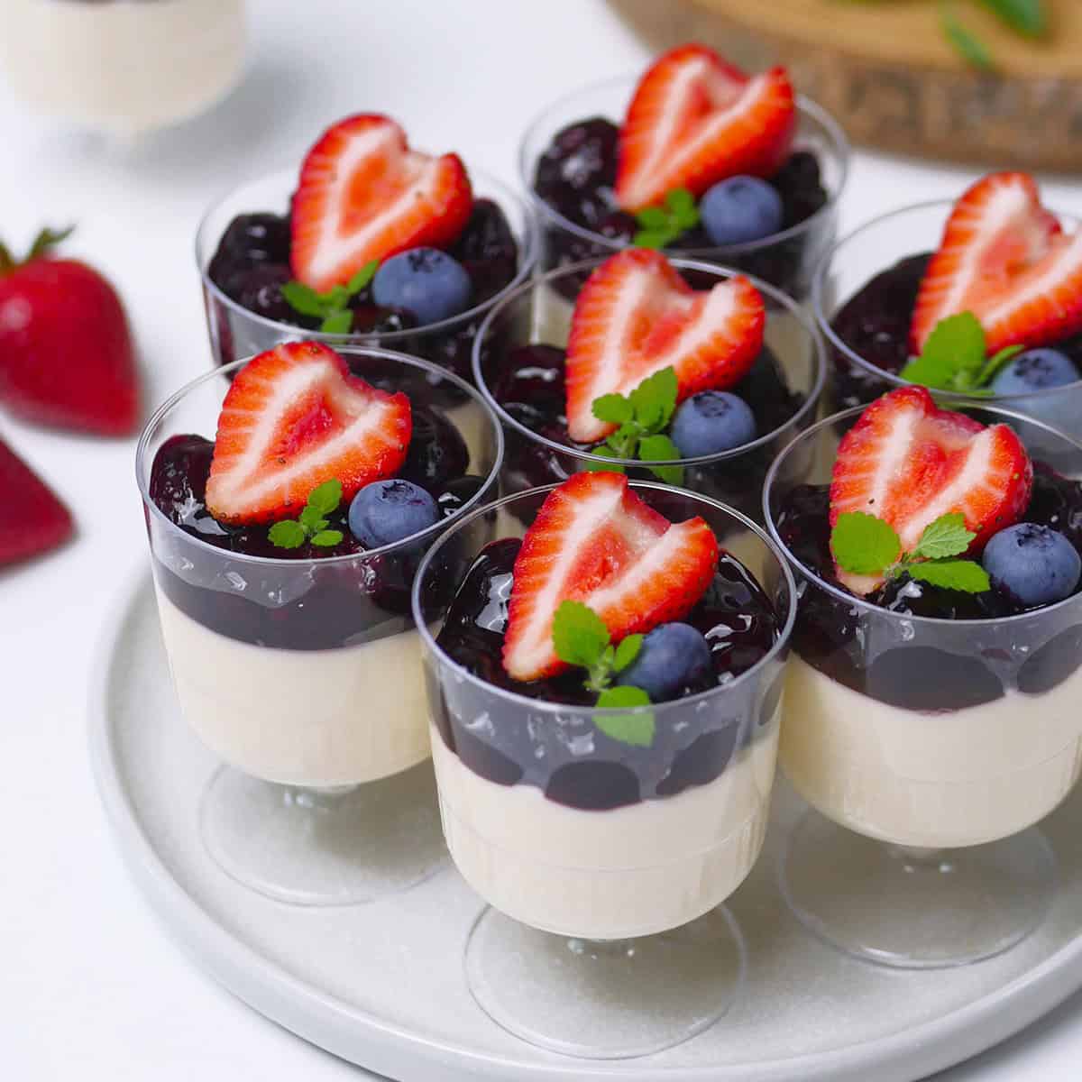 Mini berry panna cottas on a serving tray topped with strawberries and blueberries.