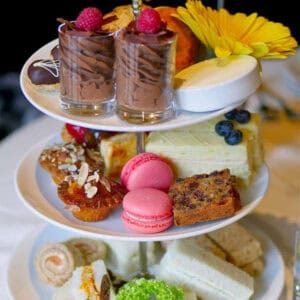 A traditional afternoon tea set on a 3-tier-tray filled with chocolate mousse, macarons, financiers and mini sandwiches.