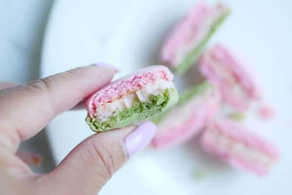 A strawberry basil macaron that's bit into, showing a full fluffy shell. 