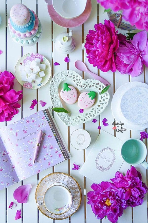 Overhead shot of strawberry macarons with tea ware and stationary.