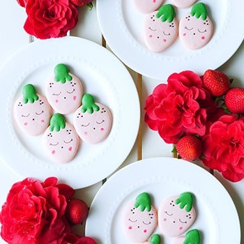 Strawberry shaped macarons on 3 different plates.