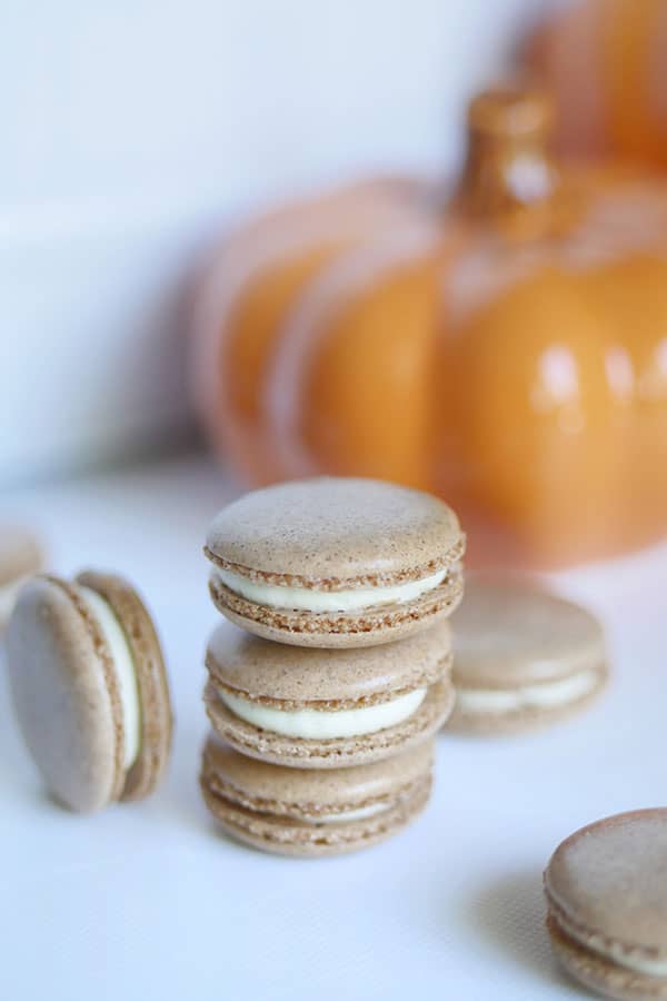 A stack of pumpkin spice cheesecake macarons in front of a pumpkin. 