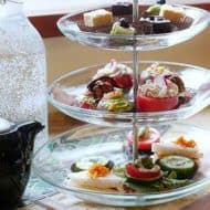 Vegan afternoon tea treats served on a clear glass 3-tier tea tray.