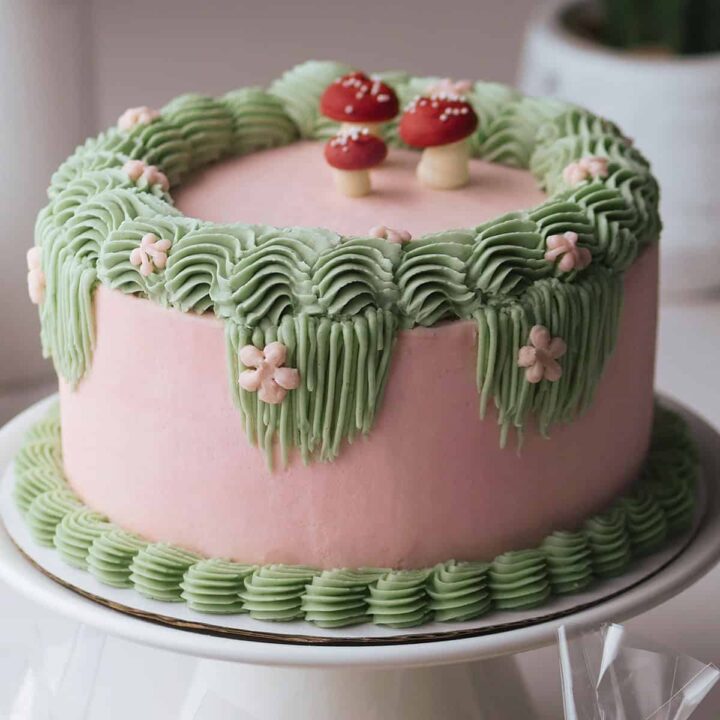 Fairy themed birthday cake decorated with Swiss meringue buttercream in mushroom shapes, flowers and thick sculpted borders.