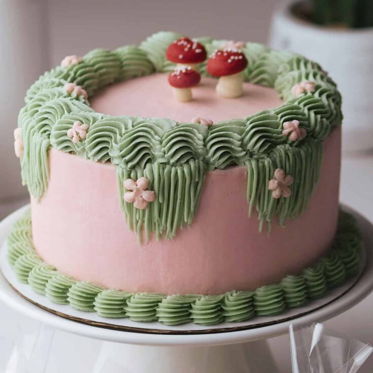 Fairy themed birthday cake decorated with Swiss meringue buttercream in mushroom shapes, flowers and thick sculpted borders.
