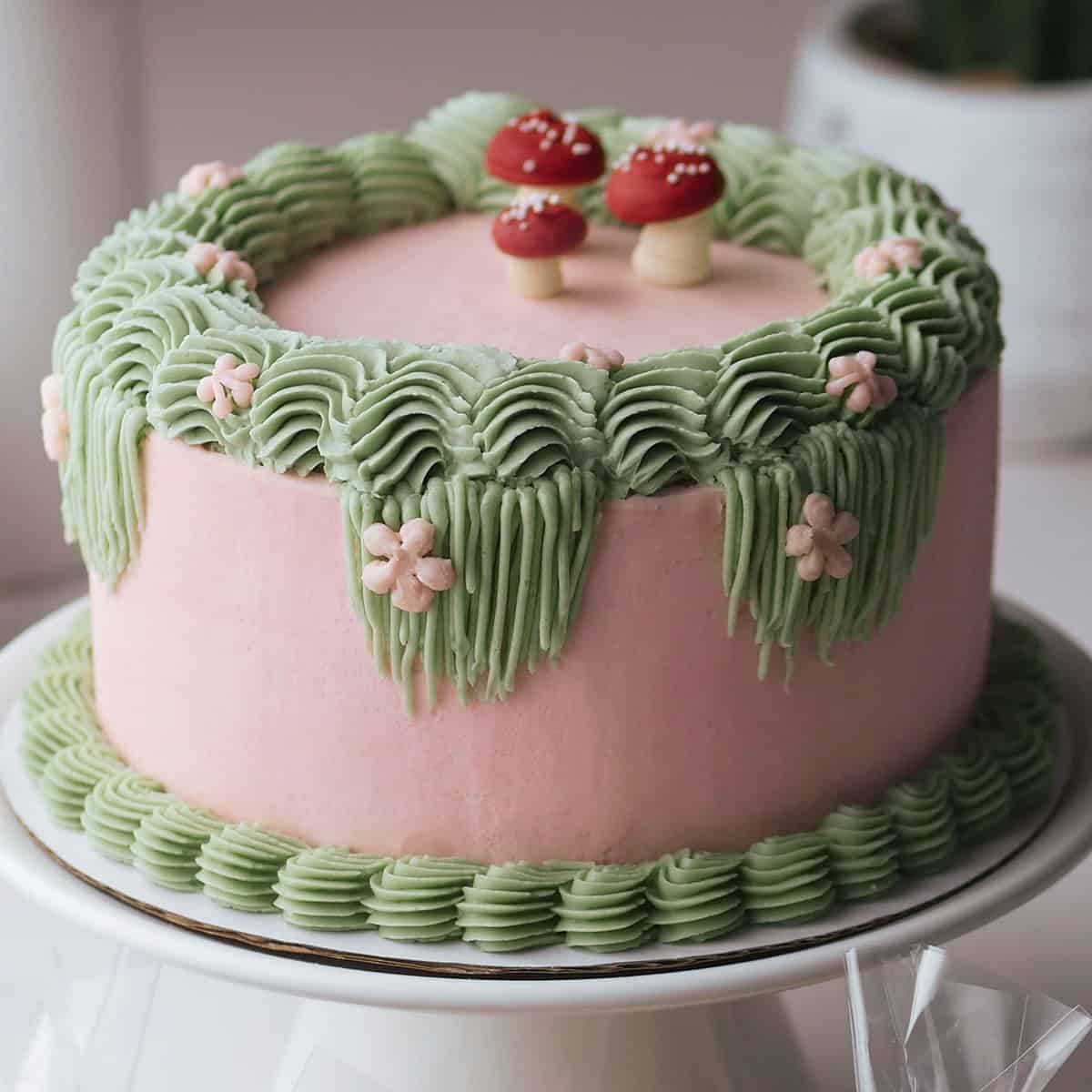 Fairy themed birthday cake decorated with Swiss meringue buttercream in mushroom shapes, flowers and thick sculpted borders.