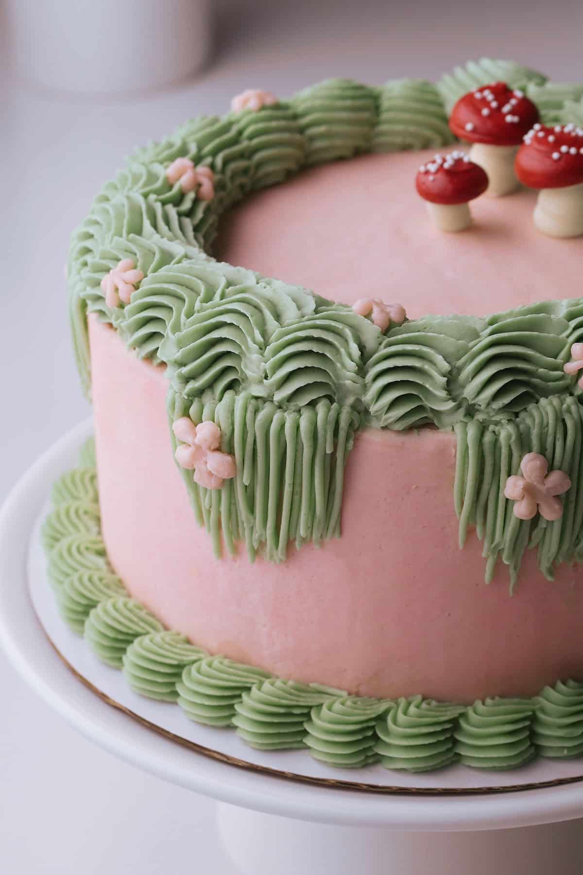 Side profile of birthday cake decorated with swiss meringue buttercream displaying shapes of flowers, borders and mushrooms.