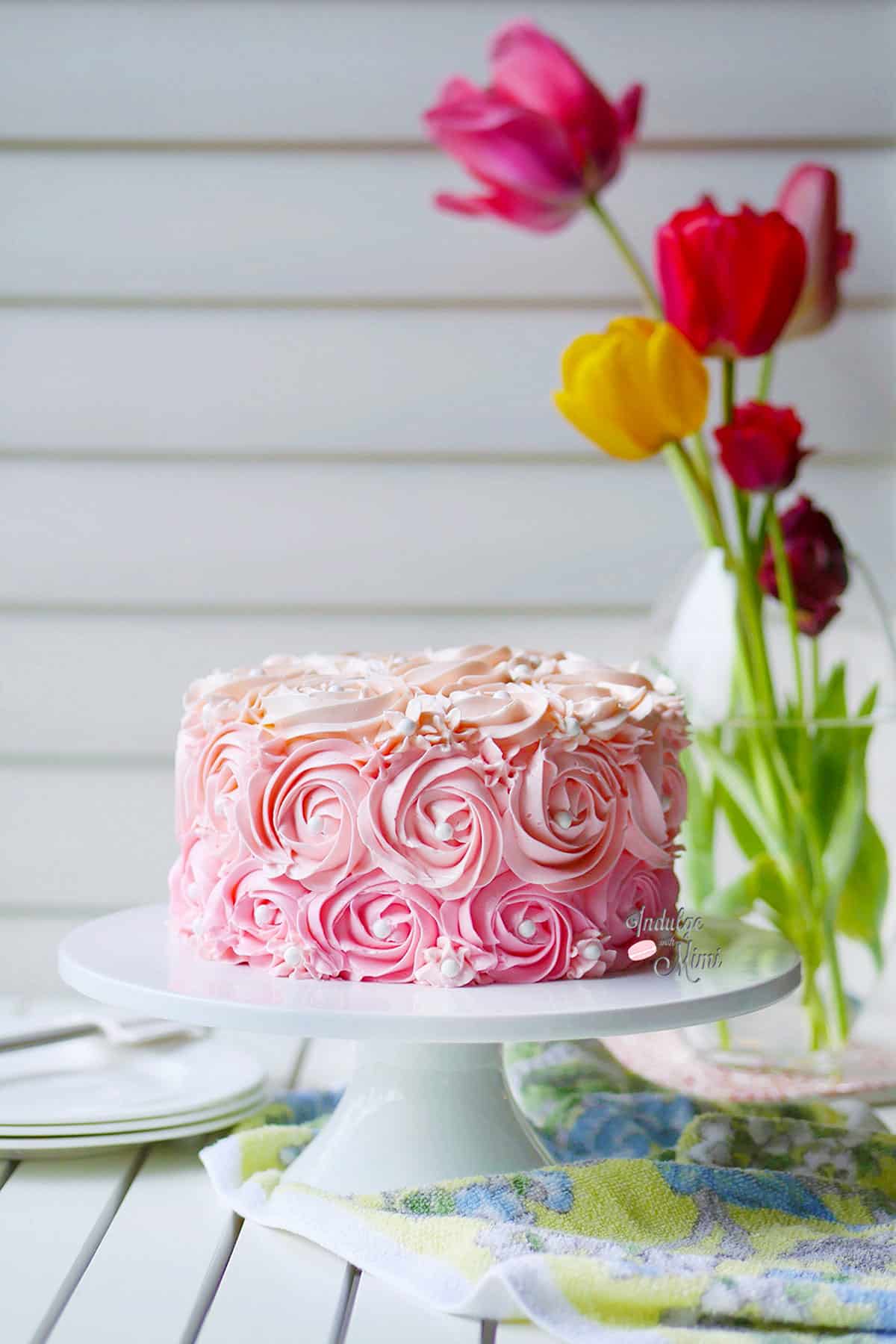 Swiss buttercream piped onto a cake in rossette pattern perched on top of a minimalistic white cake stand. 