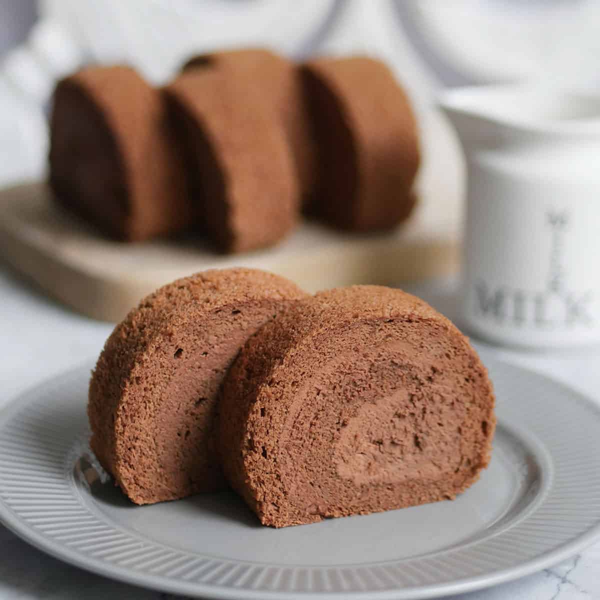 Close up of 2 slices of chocolate cake roll on a plate with some slices in the back.