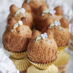 Totoro cream shaped cream puffs adorned with little flowers and leaves on a mirrored plate.