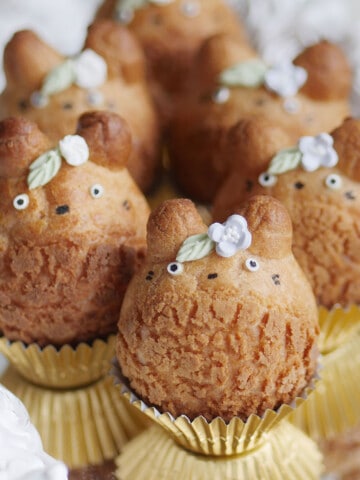 Totoro cream shaped cream puffs adorned with little flowers and leaves on a mirrored plate.