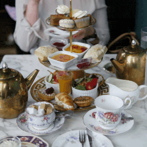 A 3-tier afternoon tea tray with gold accents filled with little treats like macarons, croissants and other tea foods.