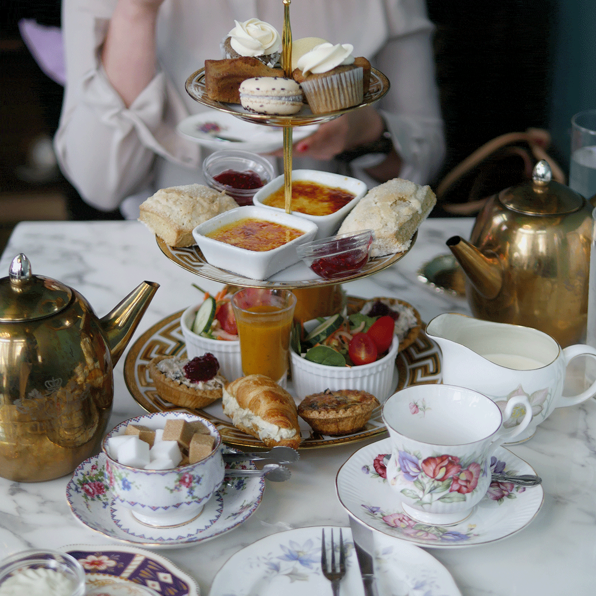 A 3-tier afternoon tea tray with gold accents filled with little treats like macarons, croissants and other tea foods.