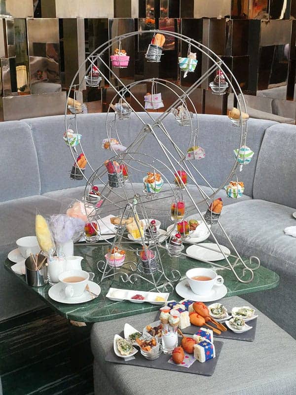 A large ferris wheel display is set on a low table with afternoon tea treats on it. 