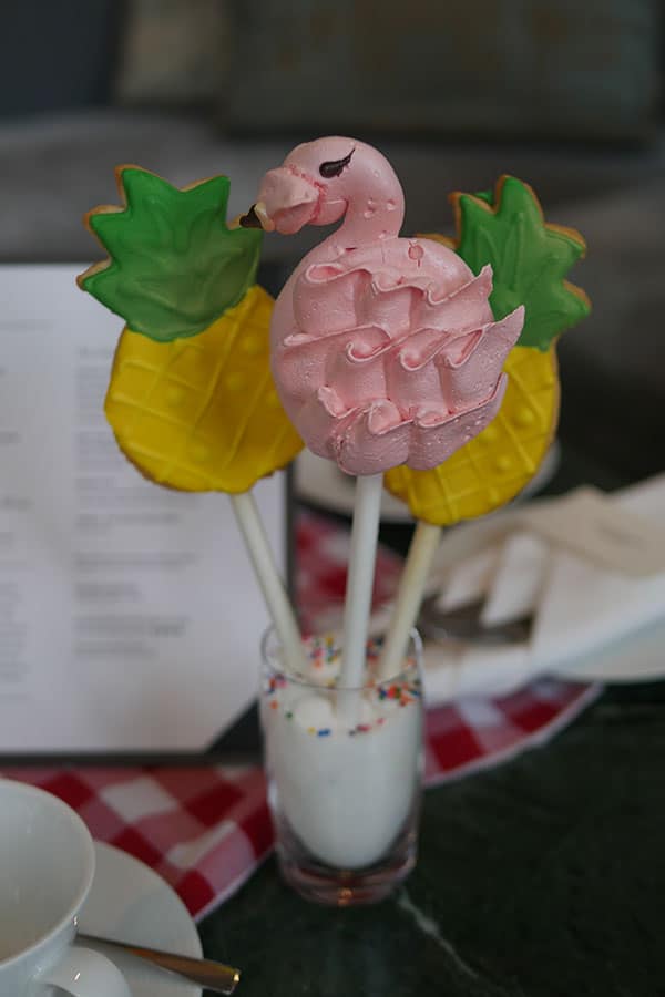 Flamingo shaped meringues with a pineapple cookie both on a stick.