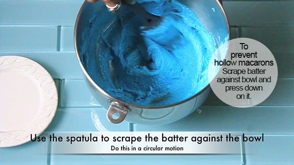 Macaron batter is being mixed with a spatula during the macaronage stage of making macarons. 