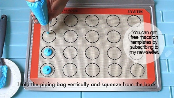Macaron batter is piped onto a silicone mat with circles. 