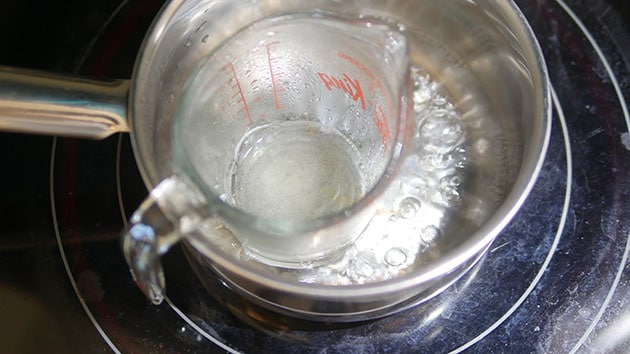 Measuring cup in a hot water bath with gelatin inside it.