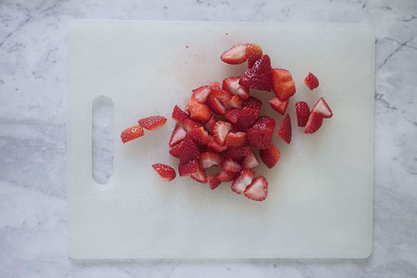 Cut up strawberries on a cutting board.
