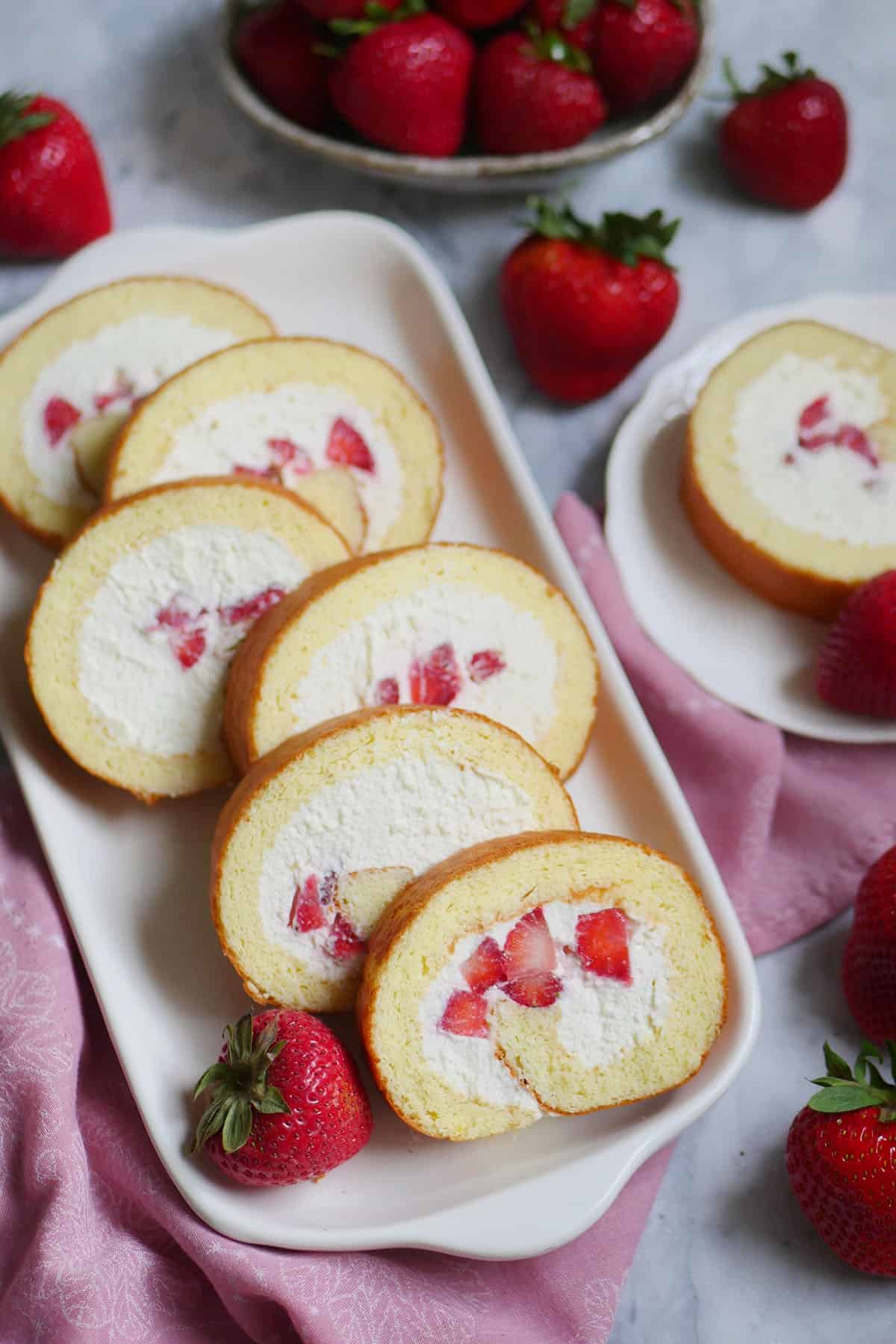 Fresh strawberry and cream Japanese swiss cake roll. Slices spread out onto a long presentation dish.