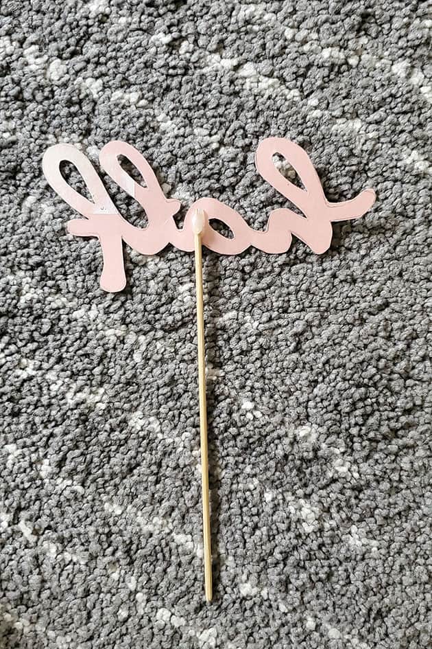 Cutout of cake topper template glued onto a long skewer..