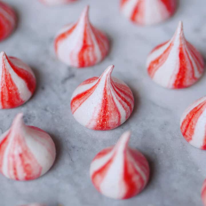 Red candy-striped meringue spaced apart on a marble counter.