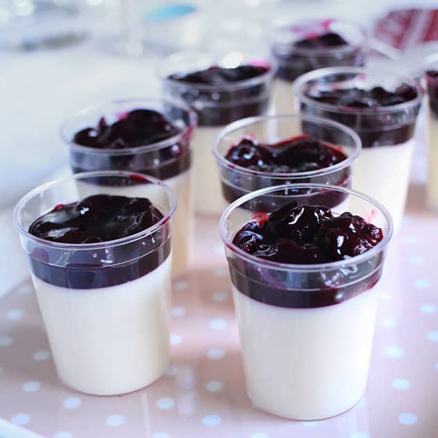 Mixed berry panna cotta in plastic shooter glasses on a pink tray for a dinner party.