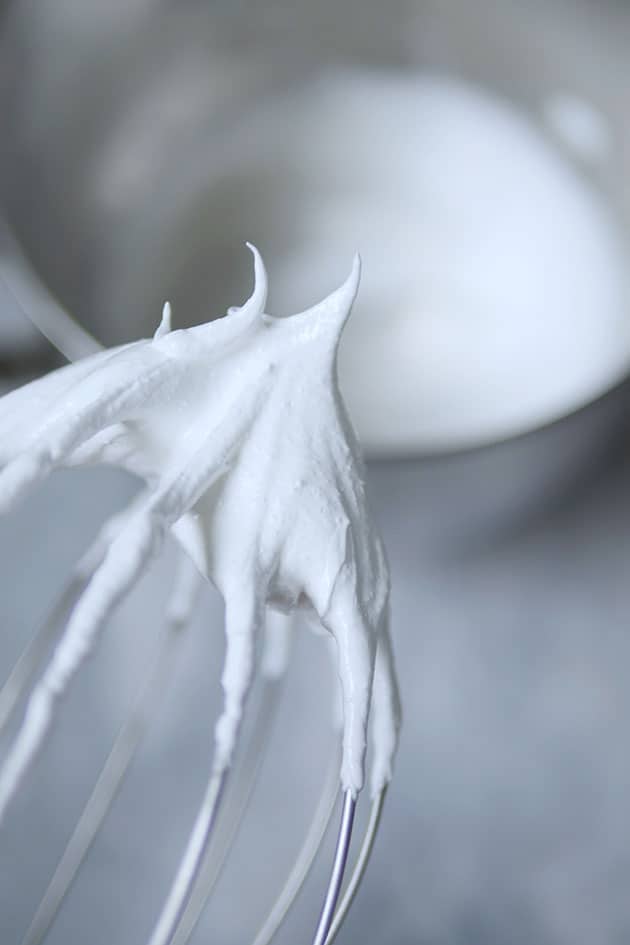 Meringue clumped inside a ball whisk with stiff pointy peaks.