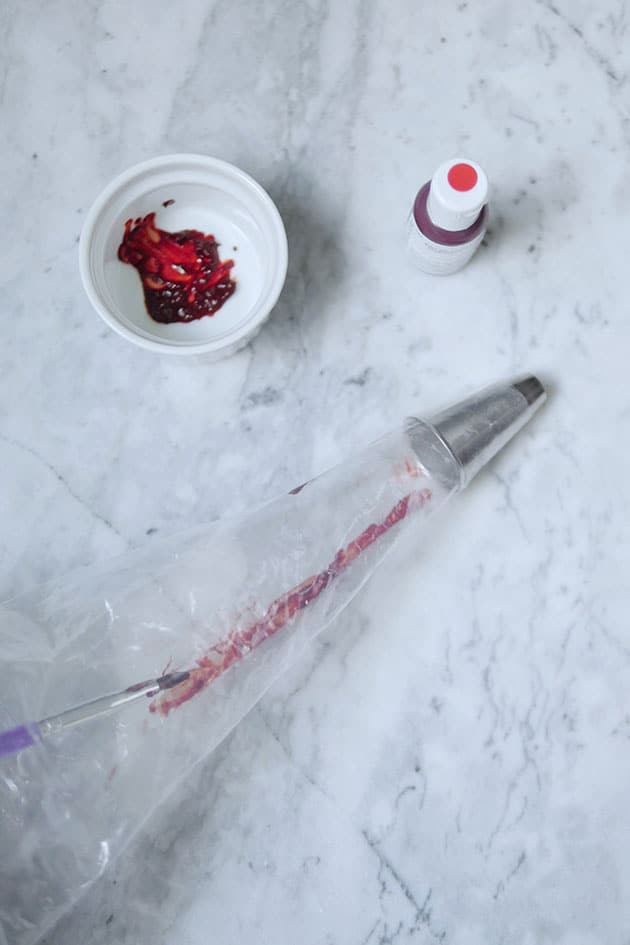 A paintbrush drawing a red line inside a piping bag with food coloring.