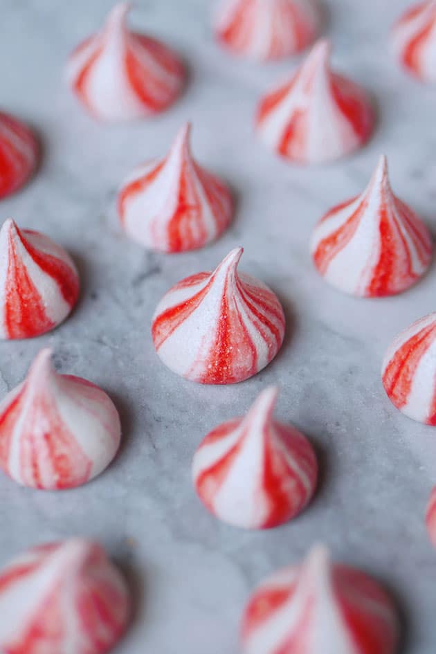 Striped meringue cookies spaced apart on marble counter. 