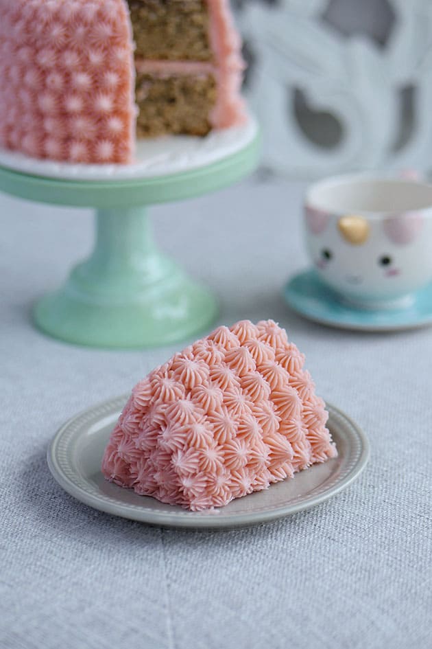 A slice of pink smash cake on a small plate in front of a whole mini strawberry banana cake with a slice cut out. 