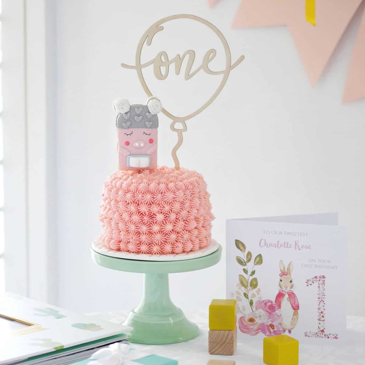 A decorated smash cake on a cake stand with a birthday card on the side.