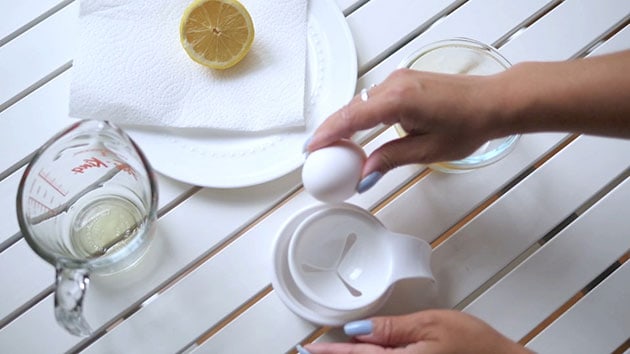 Hand is cracking an egg over an egg separator. 