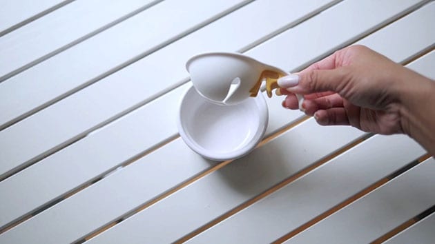 Hand is lifting an egg separator out of the bowl. 