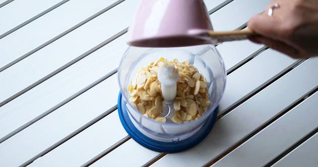 Pouring blanched almond slices into a food processor. 