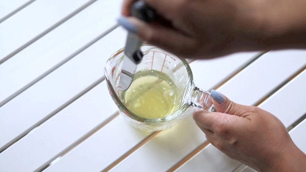 Hand puncturing plastic wrapped measuring cup filled with aged egg whites. 