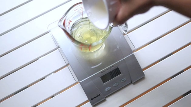 Hand is pouring egg whites into a measuring cup placed on a scale. 