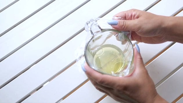 Plastic film is being stretched over a measuring cup filled with egg whites. 