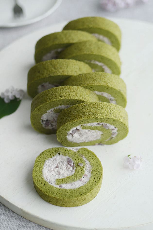 Green tea swiss roll cut into 8 slices and placed slightly apart on a white presentation board. 