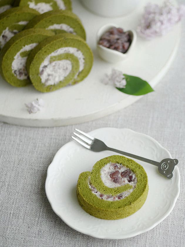 A slice of matcha cake roll on a plate with some more slices in the back. 