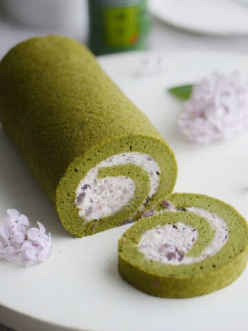 Matcha green tea cake roll with a slice cut out showing the red bean cream inside.