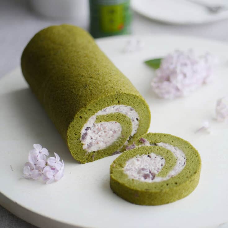 Matcha green tea cake roll with a slice cut out showing the red bean cream inside.