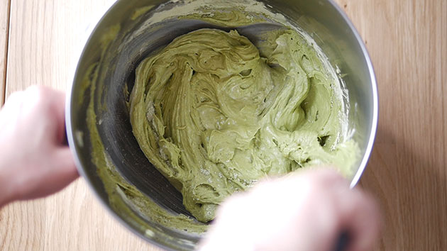 Hands scraping down batter from the side of the bowl with spatula. 