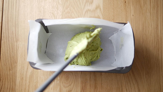 Adding matcha pound cake batter into a cake pan lined with parchment paper. 