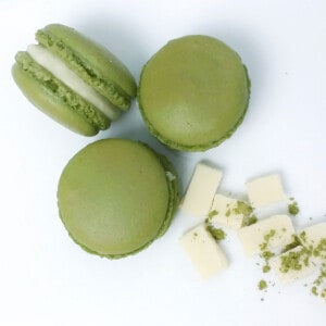 Green tea matcha macarons on a plate with some white chocolate chunks and tea powder on the side.