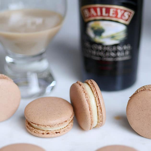 Gingerbread Baileys Irish Cream macarons on a table with a bottle of Baileys in the back.