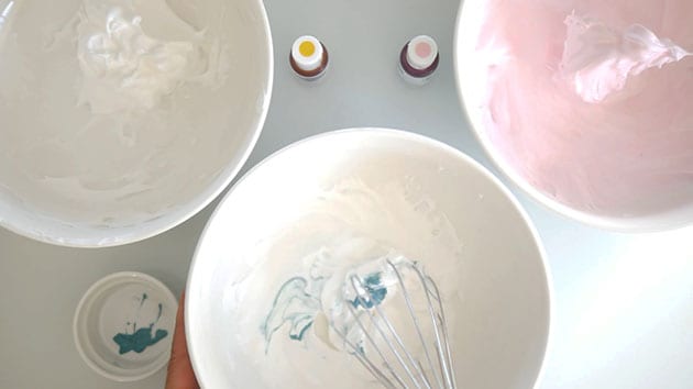 A whisk is whisking color into meringue in a bowl. 
