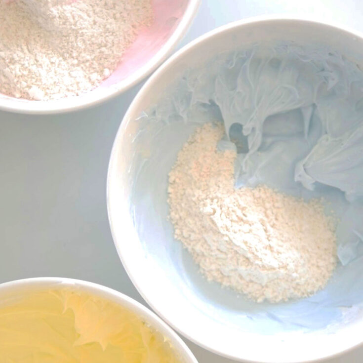 3 different colored bowls with meringue and almond flour inside to make different colored macaron batter in one batch.